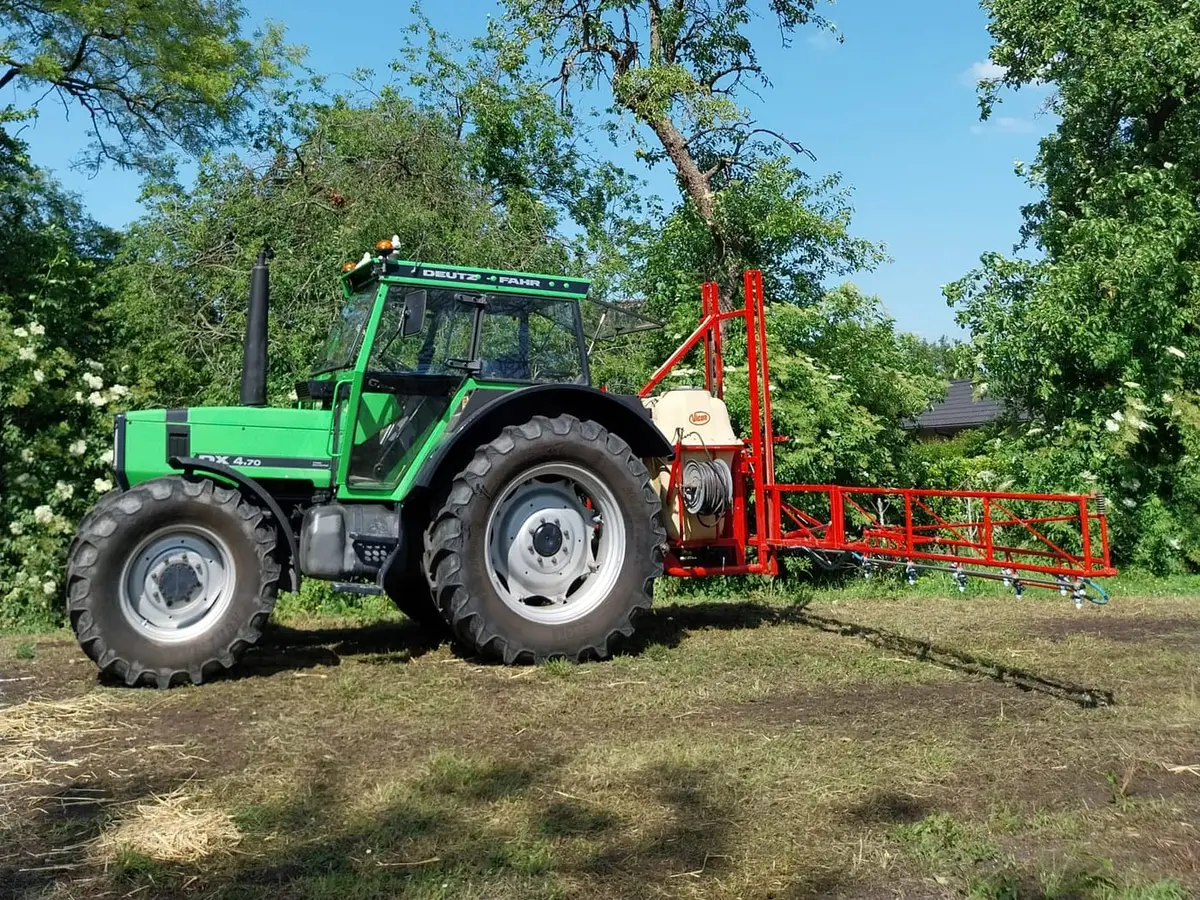 Trekker met veldspuit en uitgeklapte spuitboom langs een perceel